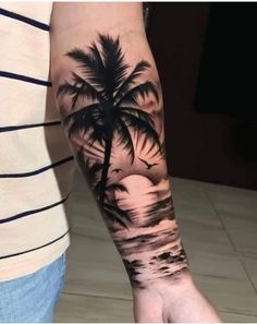 a man with a palm tree tattoo on his arm and hand is standing in front of the ocean