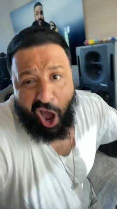 a man with a beard and white shirt making a surprised face while sitting on a bed