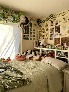 an unmade bed with stuffed animals on it in a bedroom decorated with plants and pictures