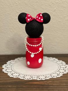 a red jar with a minnie mouse head on it and pearls around the neck, sitting on a doily