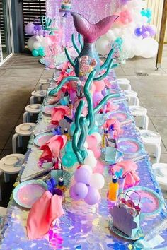 a long table covered in lots of balloons and other items for a mermaid themed party