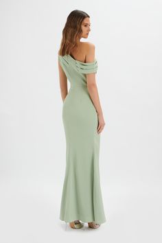 a woman in a long green dress with one shoulder and open back, looking down at the