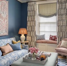 a living room with blue walls and pink furniture in the corner, along with two windows