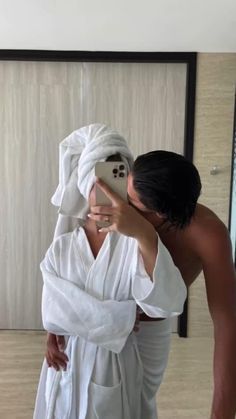 a man taking a selfie in front of a bathroom mirror wearing a white robe