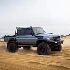 a blue truck driving on top of a dirt road in the middle of sand dunes