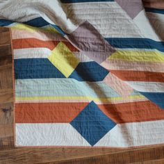 an orange, yellow and blue quilt on a wooden floor