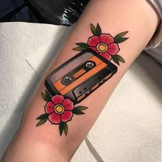 an old school style cassette tattoo on the left arm with flowers and roses around it