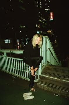 a woman standing on the side of a bridge at night with her hands in her pockets