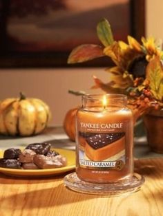 a candle sitting on top of a wooden table next to a plate with chocolate covered cookies