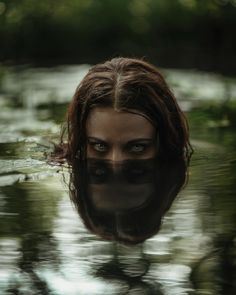 a woman's face is reflected in the water with trees and leaves behind her