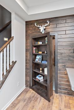 an open bookcase in the corner of a room with wooden floors and walls, along with a deer's head mounted on the wall