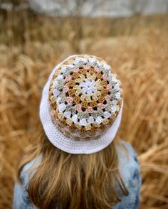 a woman wearing a crocheted hat standing in a wheat field with her back to the camera