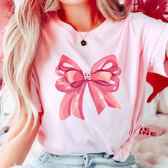 Embrace elegance and flirtatious charm with our captivating pink bow shirt, a delightful addition to your coquette-inspired wardrobe! 🌸👚 This shirt embodies the essence of femininity and playfulness, perfect for those who adore a touch of chic sophistication with a hint of flirtation. 🌷 The darling pink hue complements the shirt's design, accentuating the focal point--an exquisitely crafted oversized bow adorning the neckline or sleeves, adding a whimsical and flirtatious allure to your ensem Pink Tops With Bow For Party, Pink Party Top With Bow, Feminine Party Tops With Bow Detail, Cute Pink T-shirt With Bow, Cute Party Tops With Bow, Cute Party Tops With Bow Detail, Pink Party Shirt For Spring, Spring Party Tops With Ribbon, Feminine Tops With Ribbon For Spring