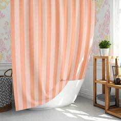 a bath tub sitting next to a window covered in a pink and white striped curtain