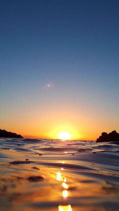 the sun is setting over the ocean with small rocks in the water and some waves