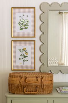 a dresser with two pictures and a basket on top of it next to a mirror