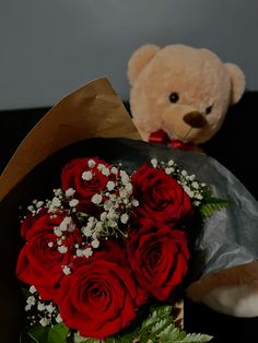 a teddy bear sitting next to a bouquet of red roses and baby's breath