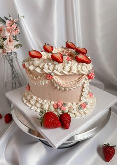 a three tiered cake with strawberries on top and flowers in the vase next to it