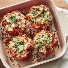 four stuffed tomatoes in a casserole dish with cheese and herbs sprinkled on top