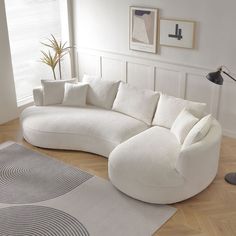 a large white couch sitting on top of a wooden floor next to a lamp and rug