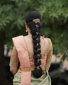 a woman with long black hair wearing a pink and green saree, braided into a ponytail