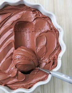 a white bowl filled with chocolate frosting on top of a wooden table next to a knife