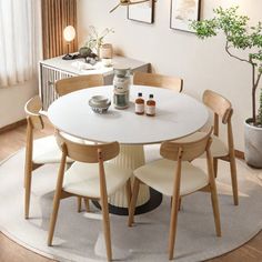 a white table with four chairs around it in a living room next to a potted plant