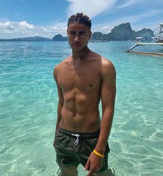 a shirtless man standing in shallow water near the ocean with his hands on his hips