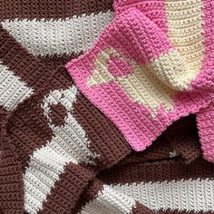 a crocheted blanket is laying on top of another knitted blanket with a pink and brown design