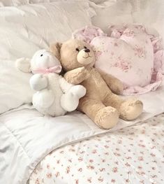 two teddy bears sitting on top of a bed next to pillows and sheets with pink flowers