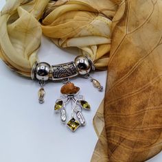 GENUINE GEMSTONE SCARF PENDANT WITH COORDINATING SCARF A soft yellow background with golden yellow and beige flowers in the foreground form the design for this long floral themed scarf. This beautiful scarf pairs with a coordinating gemstone scarf slide pendant of golden citrine and white pearls  to complement the flowers in the scarf design STATEMENT GEMSTONE SCARF PENDANT WITH 4 SCARF RINGS This multi-gem statement pendant begins with a natural citrine geode gemstone, followed by stations of natural white pearls and faceted golden citrine, all in a silver filigree setting.  The scarf pendant bail theme is a floral design to show your love of nature.  The pendant measures 2-½ inches long x 2 inches wide. The set also comes with four scarf rings-two coordinating crystal charm scarf rings a Gold Citrine Jewelry With Stones, Yellow Birthstone Pendant Jewelry, Bohemian Amber Jewelry With Gemstone Accents, Yellow Natural Stones Jewelry As A Gift, Handmade Yellow Citrine Jewelry, Amber Citrine Dangle Jewelry, Unique Yellow Gemstone Jewelry, Yellow Metal Pendant Jewelry, Bohemian Yellow Gemstone Jewelry