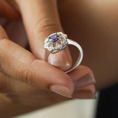 Sometimes when a girl says she likes to receive flowers as a gift, it's not the real flowers she meant. Think twice and go for the safest thing - our Flora ring with amethyst and side Moissanites. Floral jewelry is where it's at! Perfect as a graduation gift, birthday gift, anniversary ring, or a promise ring. Details: Center stone Gemstone: Amethyst Stone Shape: Round Measurements: 5.00mm Side stones Gemstone: Moissanite Shape: Round Measurements: 1.30mm (8) Band measurements: approx. 1.8mm wid Flower Shaped Promise Ring With Birthstone, White Gold Flower Ring With Birthstone For Wedding, Elegant Purple Flower Ring As A Gift, Flower Shaped Gemstone Rings For Gifts, Flower Shaped Gemstone Ring Gift, Elegant Purple Flower Ring As Gift, Elegant Purple Flower Ring For Gift, Flower Shaped Birthstone Rings For Gift, Sterling Silver Flower Ring With Birthstone For Gift