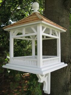 a white bird feeder hanging from the side of a tree