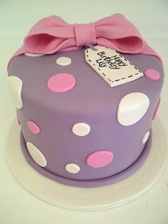 a purple cake with white polka dots and a pink bow on top that says happy birthday