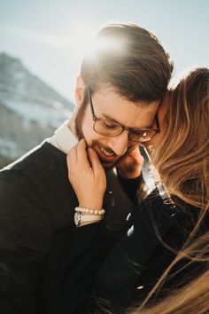 a man and woman embracing each other in front of snow covered mountain range with sunlight shining on them