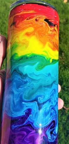 a hand holding a colorful glass in the grass