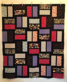 a quilt hanging on the wall with many different colors and patterns in it, including red, purple, blue, and black