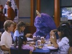 people sitting around a table eating food with an animal in the background