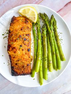 a white plate topped with fish and asparagus next to a lemon wedged slice