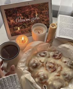 a person is holding a cup and looking at a book with cinnamon rolls on it