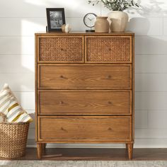 a wooden dresser with wicker drawers in a white room next to a basket and clock