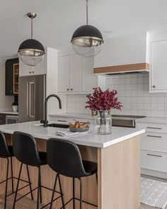 a kitchen with white cabinets and black bar stools, two pendant lights over the island