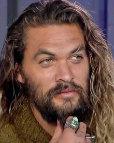 a close up of a person with long hair and a ring on his finger in front of him