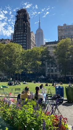 people sitting on benches in the middle of a park with tall buildings in the background