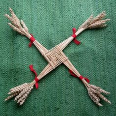 a cross made out of straw with red ribbon around it sitting on a green surface