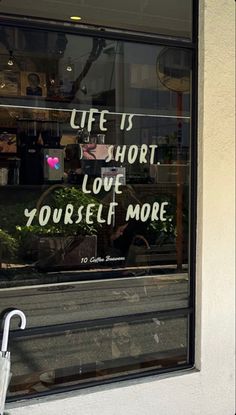 a store window with an umbrella in front of it and the words life is short love yourself more