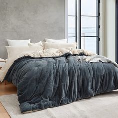 an unmade bed sitting in front of a large window next to a wooden floor