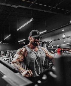 a man in grey shirt and black hat working out at a gym with other people