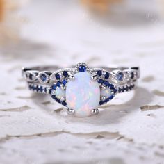 6x8mm Oval cut opal engagement ring set in white gold. The stones are Opal and lab blue sapphire. The center opal is about 6x8mm Oval Cut. The stones can be replace with other gemstones.For example,if you don't like the CZ accent,you can ask me replace it with tourmaline,aquamarine,diamond,emerald,sapphire... For custom making jewelry,it can be made in 2 different metal. 1,Solid gold,including 14/18k white/rose/yellow gold. 2,925 sterling silver with white/yellow/rose gold plated. High quality w Blue Sapphire Wedding Ring Set, Opal Wedding Ring Set, Ring Redesign, Sapphire Wedding Ring Set, White Opal Engagement Ring, Redesign Ideas, Blue Sapphire Wedding Ring, Opal Engagement Ring Set, Sapphire Wedding Rings