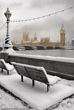 two benches covered in snow next to the river thames and big ben, london england